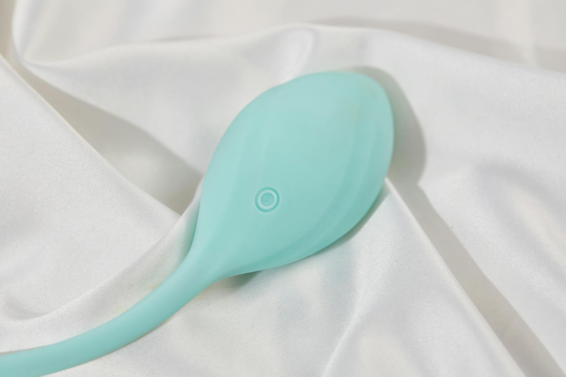 A teal clitoral vibrator on white silk fabric, representing pleasure after pelvic floor recovery.