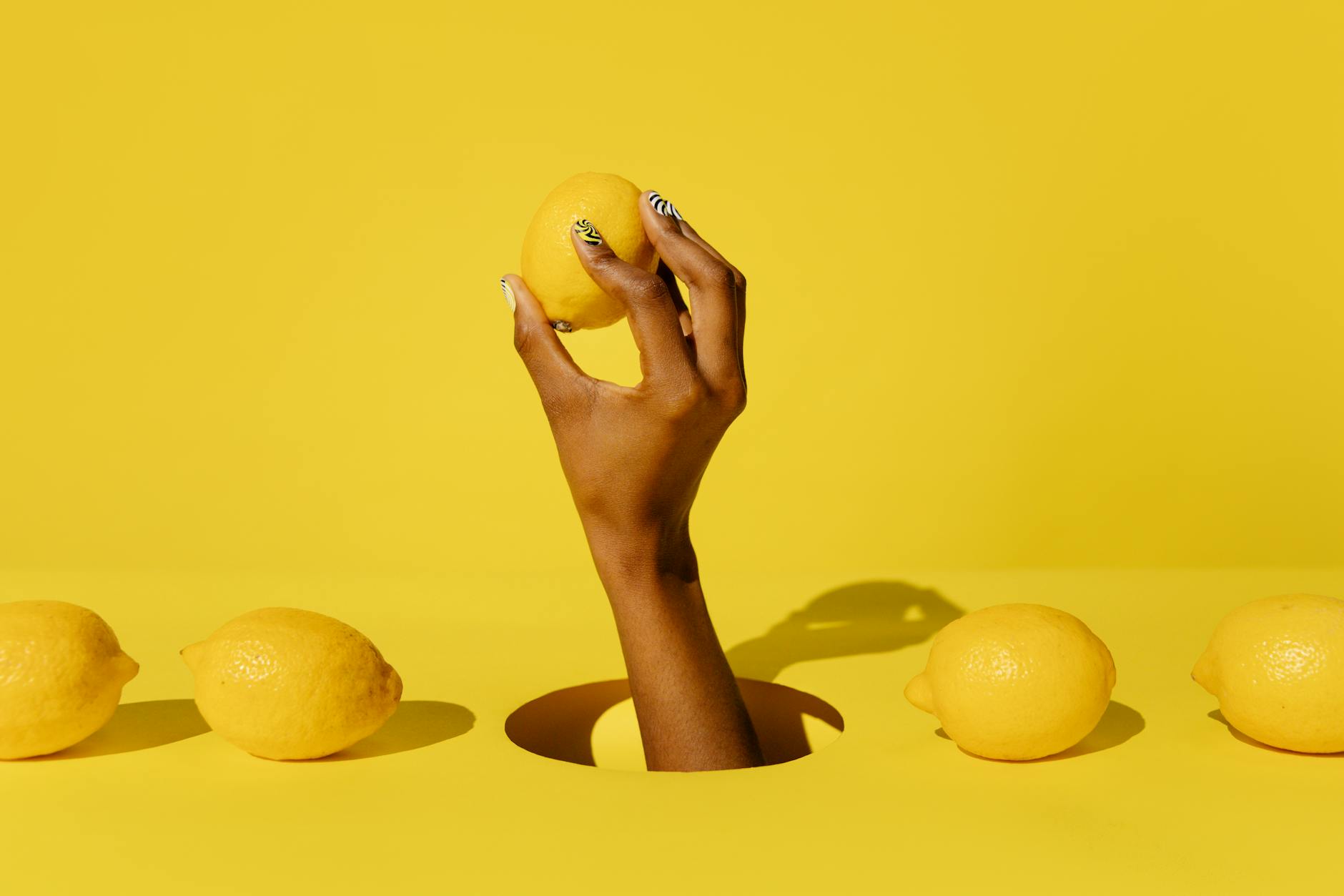A hand holding a fresh lemon against a vivid yellow background, symbolizing renewal and rediscovery of sensation