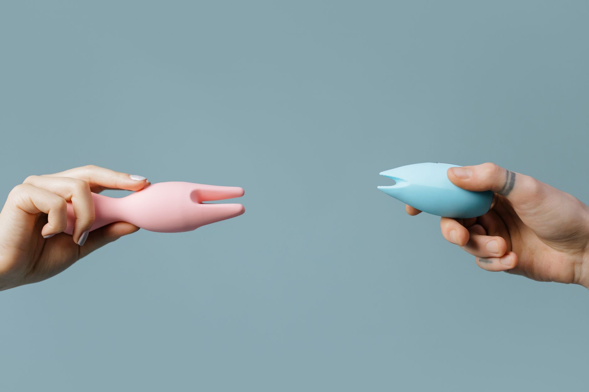 Woman holding blue and pink clitoral vibrators against a purple background.