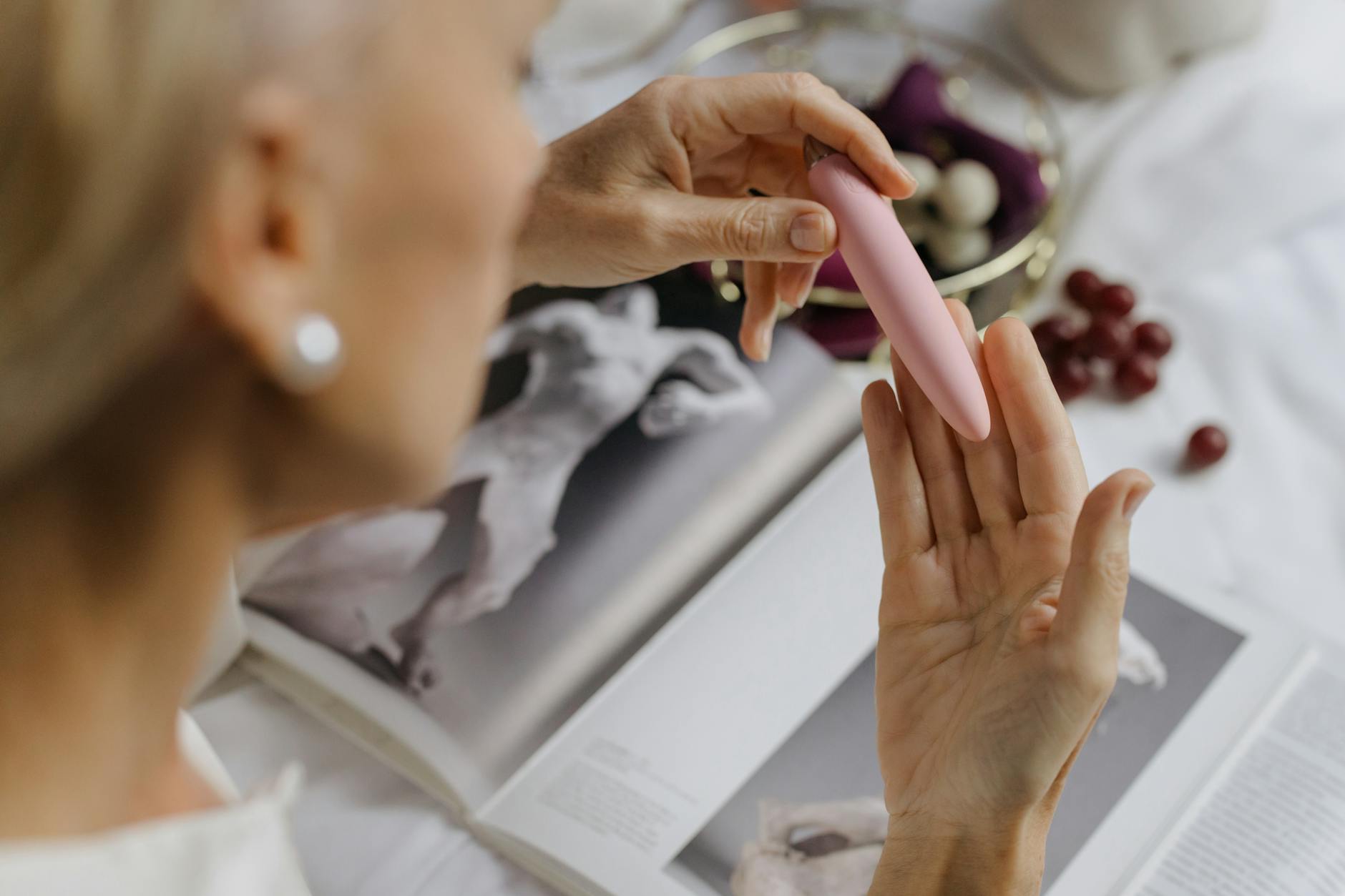 Woman holding a pink vibrator with art books nearby, symbolizing personal pleasure and intimate exploration