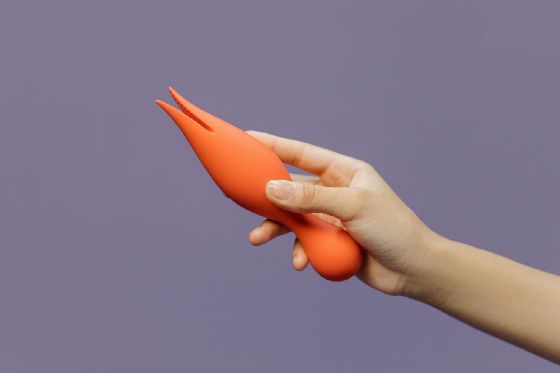 Hand holding a lemon clitoral vibrator against a minimalistic purple backdrop
