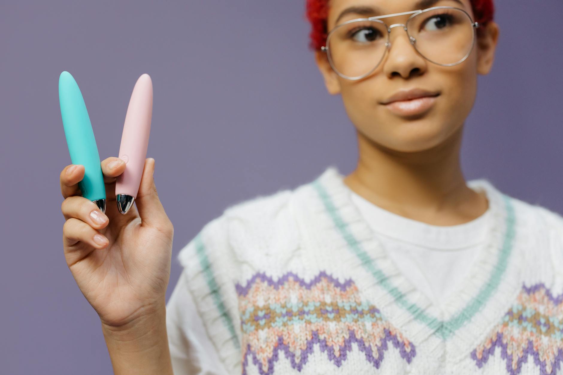 A woman holding colorful clitoral vibrators against a purple background