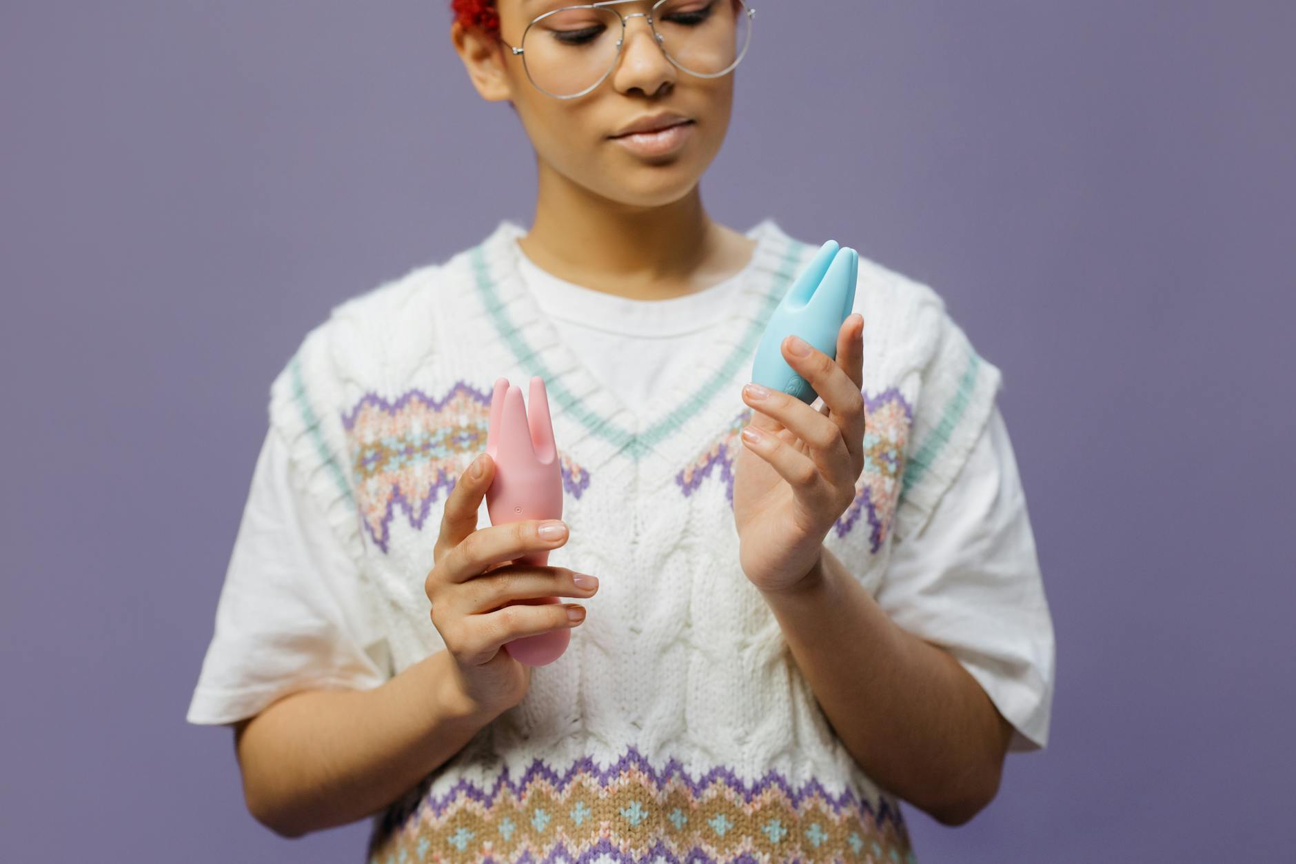 Woman holding blue and pink silicone vibrators thoughtfully, exploring pleasure with intention