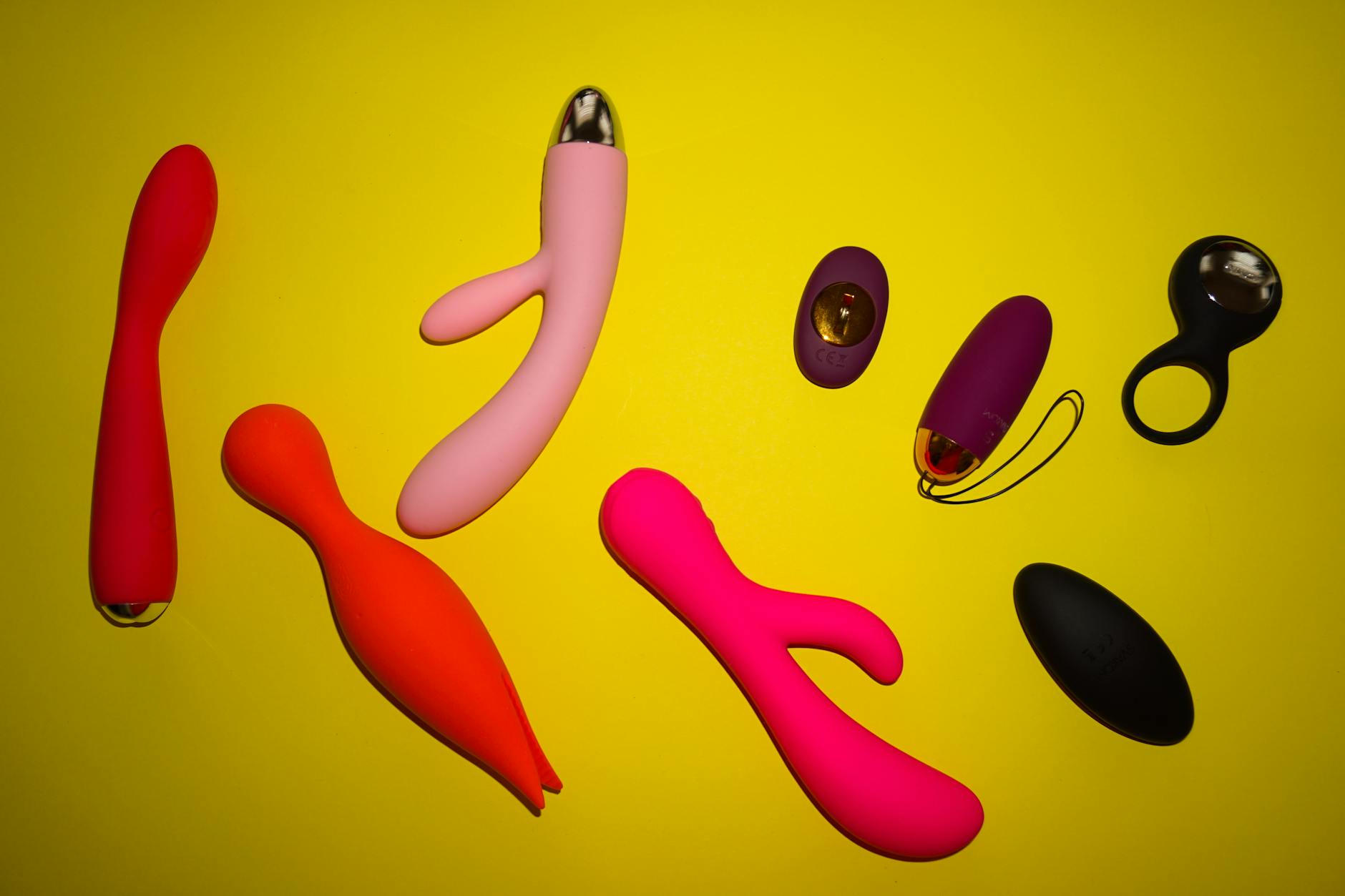 Colorful sex toys including lemon clitoral vibrators arranged on a bright yellow surface